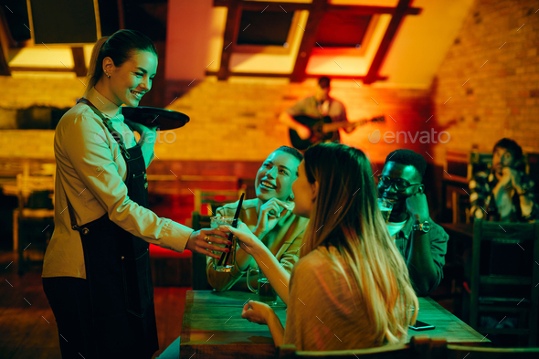 Happy waitress serving drinks to group of friends in a pub.