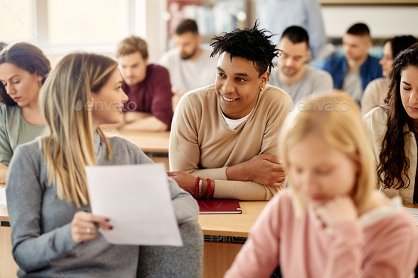 Happy African American student talking to his friend during a class at university classroom.