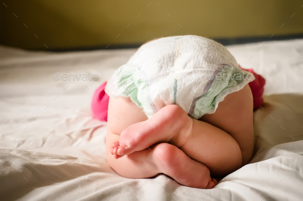 Newborn in diaper rear view. A little newborn girl sleeps on a large bed with her legs folded on top