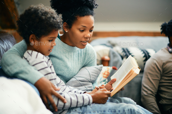 African American mother enjoying in reading a book to her son at home.