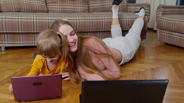 Woman Nanny and Child Girl Studying Together with Computer Laptop While Lying on Warm Floor at Home alt