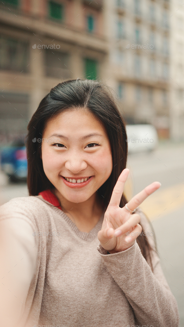 Pretty Asian girl taking self portrait showing peace sign outdoors