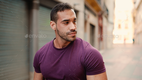 Handsome muscular man looking confident while walking down the narrow street - Stock Photo - Images