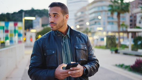 Portrait of confident man using smartphone standing on the evening city street - Stock Photo - Images