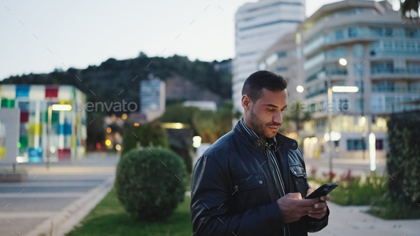 Young man wearing leather jacket checking his smartphone on the street - Stock Photo - Images