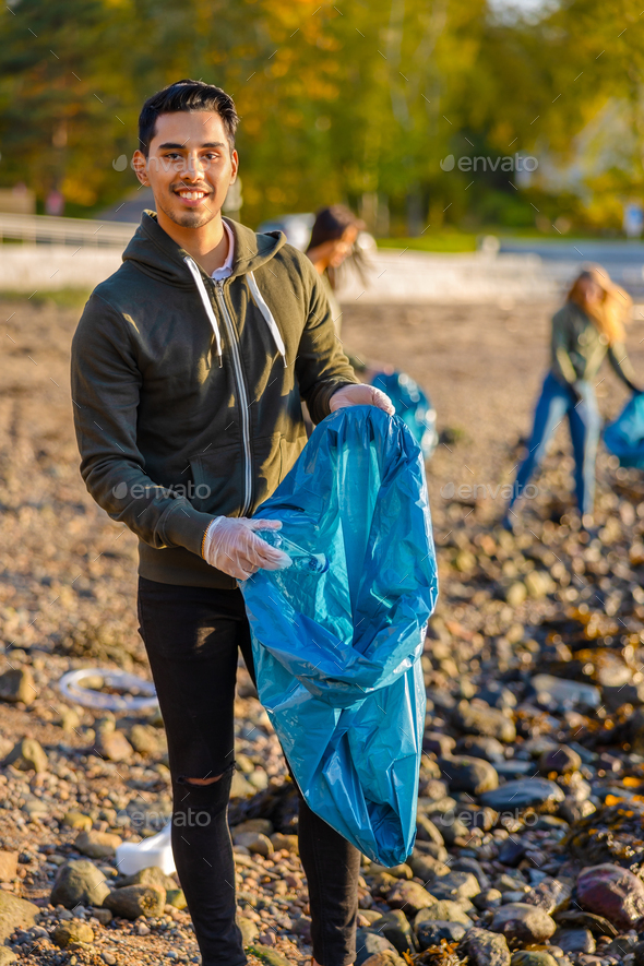 Young man collects garbage in bag with group of volunteers on sunny day - Stock Photo - Images