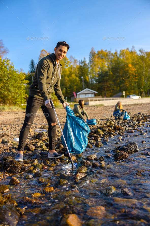Smiling young man cleaning the ocean with volunteers on sunny day