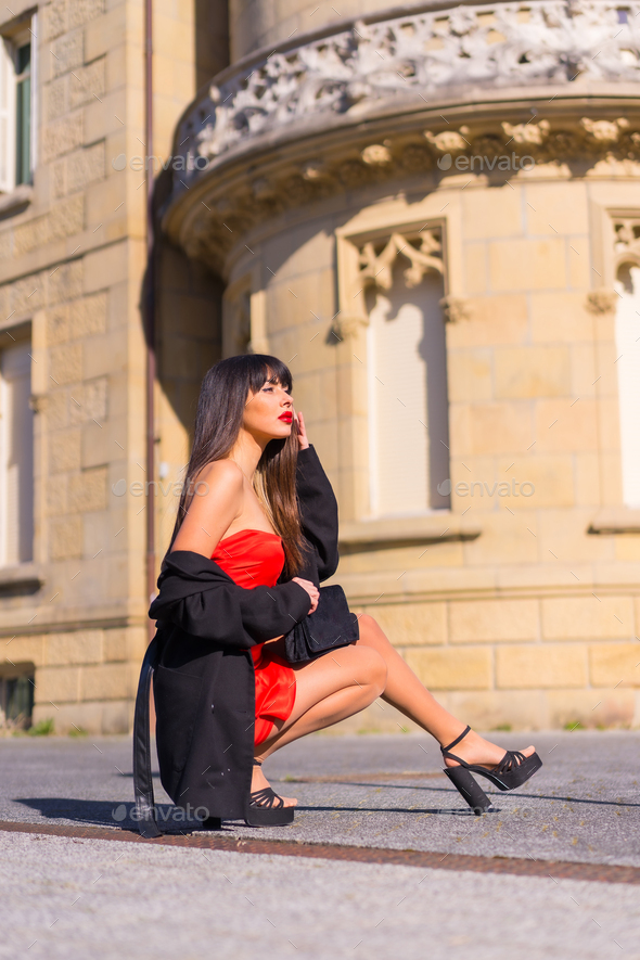 Portrait in red dress in beautiful castle, attractive girl, crouching fashion pose