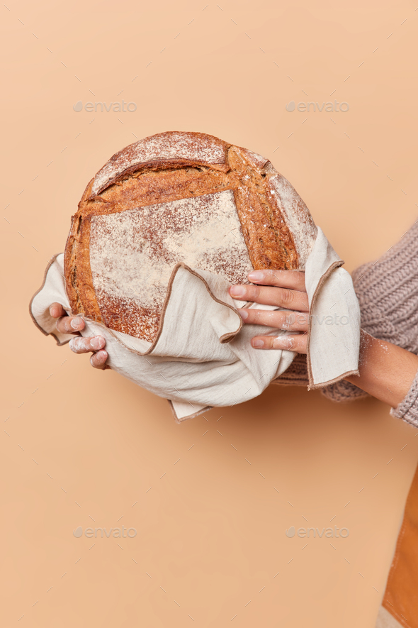 Vertical shot of unrecognizable woman holds round loaf of bread on towel isolated over beige backgro - Stock Photo - Images