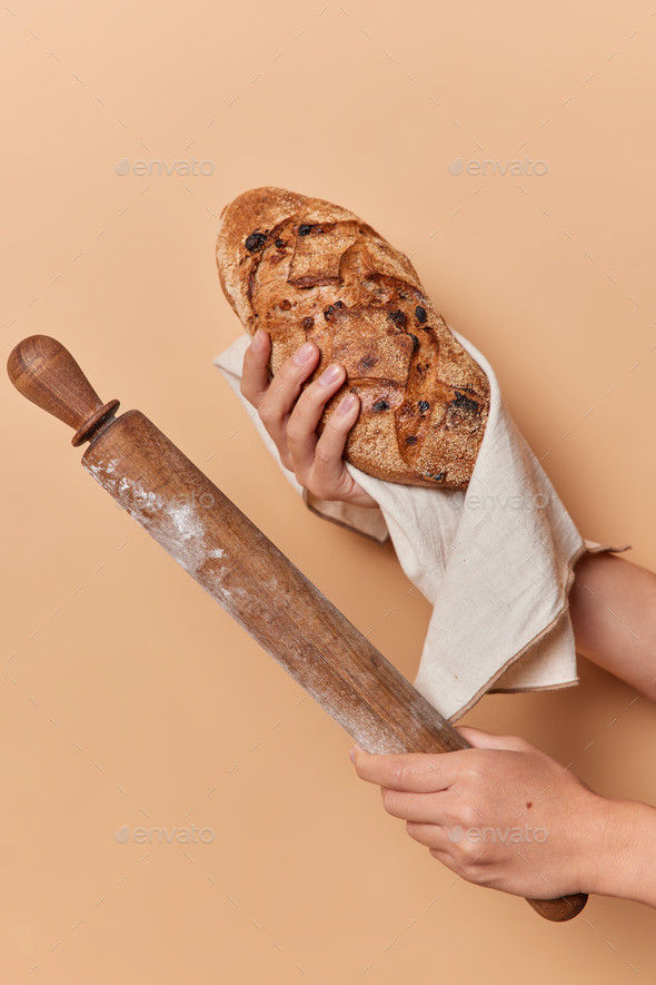 Unrecognizable person holds homemade crusty appetizing bread wrapped in linen napkin and rolling pin - Stock Photo - Images