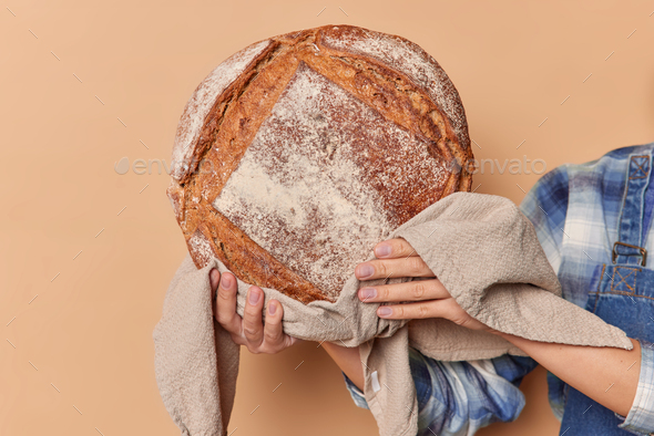 Unrecognizable woman baker holds round fragrant rye bread on linen napkin demonstrates homemade fres - Stock Photo - Images