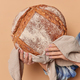 Unrecognizable woman baker holds round fragrant rye bread on linen napkin demonstrates homemade fres - PhotoDune Item for Sale