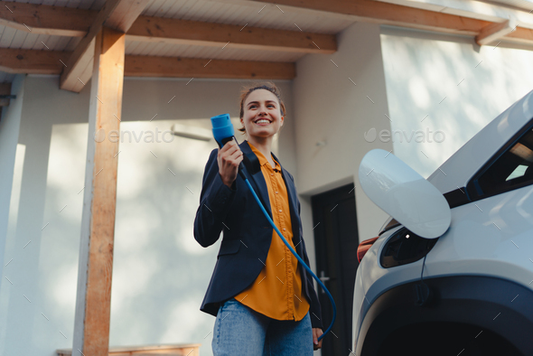 Young woman holding power supply cable from her electric car, prepared for charging it in home - Stock Photo - Images