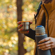 Woman backpacker holds thermos with hot beverage in hand at autumn forest - PhotoDune Item for Sale