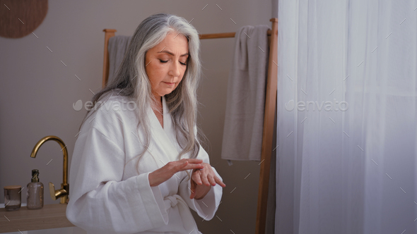 Beautiful grandma 60s lady old senior gray haired female Caucasian woman in bedroom rubbing wrinkled