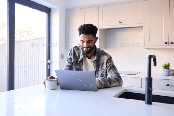 Man At Home Working On Laptop On Counter In Kitchen - Stock Photo - Images