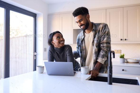 Young Couple At Home Looking At Laptop On Counter In Kitchen Together