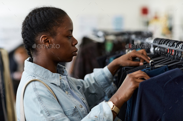 Young woman browsing clothes on racks in thrift store