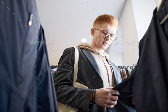 Young man browsing clothes on racks in thrift store