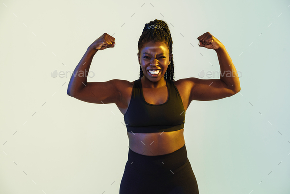 Smiling fitness woman show her biceps at gym Stock Photo by vadymvdrobot