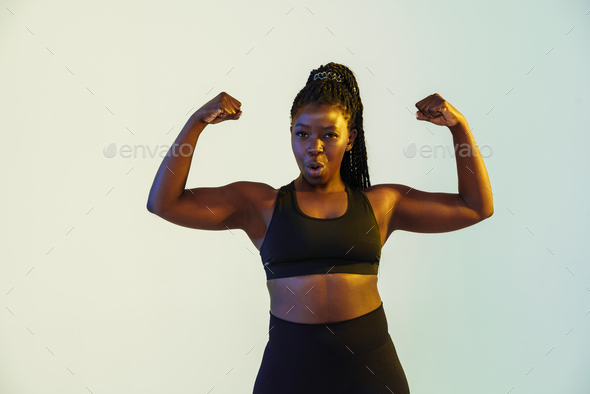 Smiling fitness woman show her biceps at gym Stock Photo by vadymvdrobot