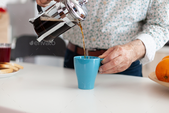 Older man spilling coffee in cup after making it using french press