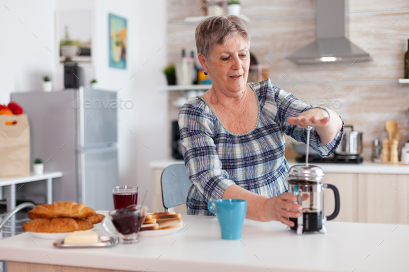 Old woman pushing down the lid of french press while making coffee
