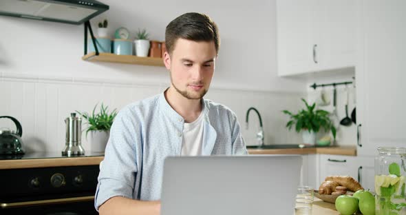 Young Confident Man Portrait. Freelancer Works on Laptop in Kitchen at Home