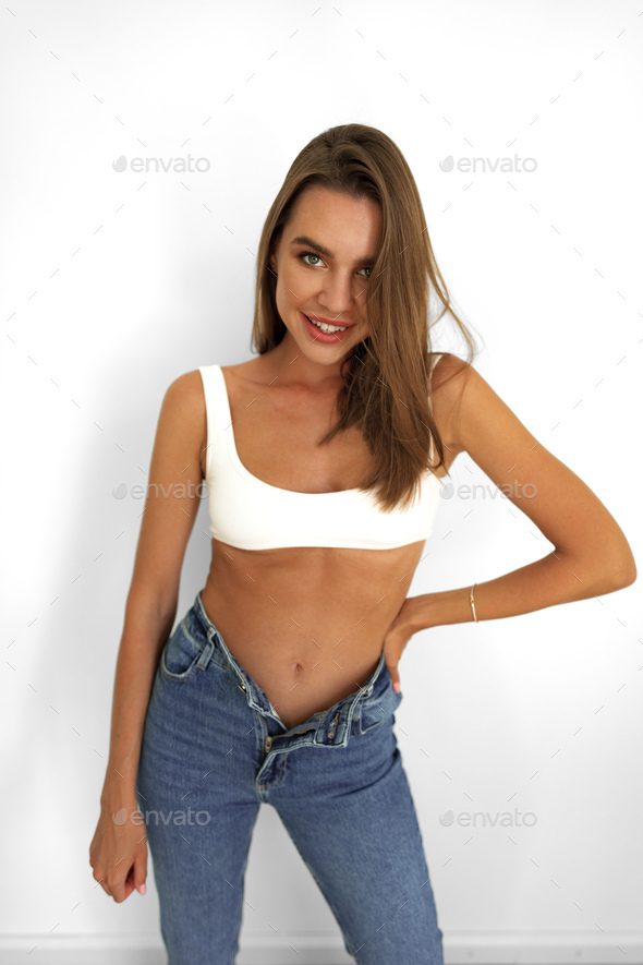 Young model woman in white underwear and jeans posing on studio background  Stock Photo by FabrikaPhoto