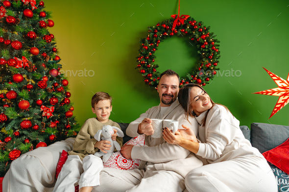 Happy young family sitting on sofa and relaxing at home at Christmas - Stock Photo - Images