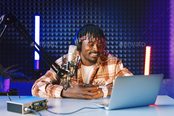 African radio host sitting at desk recording in studio with microphone and laptop - Stock Photo - Images