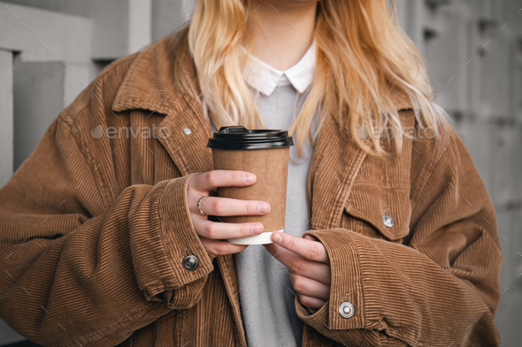 A glass of coffee in the hands of a woman in a corduroy jacket, close-up.