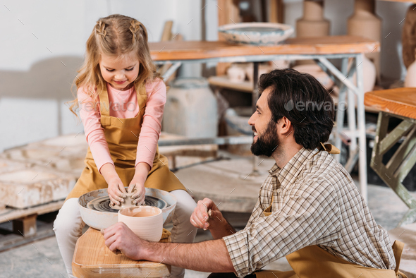 adorable kid making ceramic pot on pottery wheel with teacher