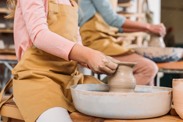 cropped view of teacher and child making ceramic pots on pottery wheels