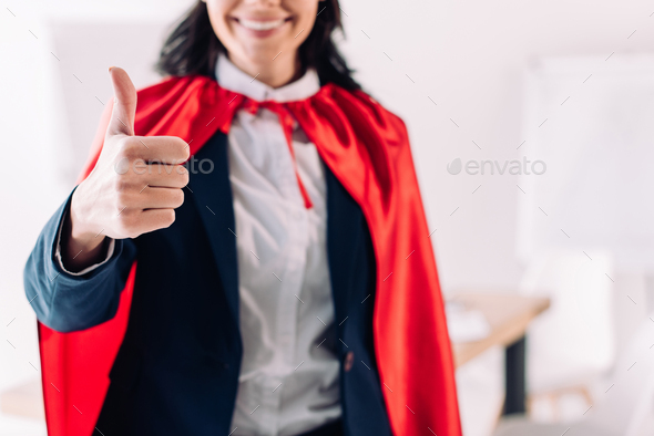 cropped image of super businesswoman in cape showing thumb up in office