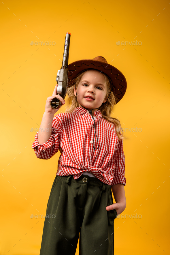 stylish cowgirl in hat with gun, isolated on yellow