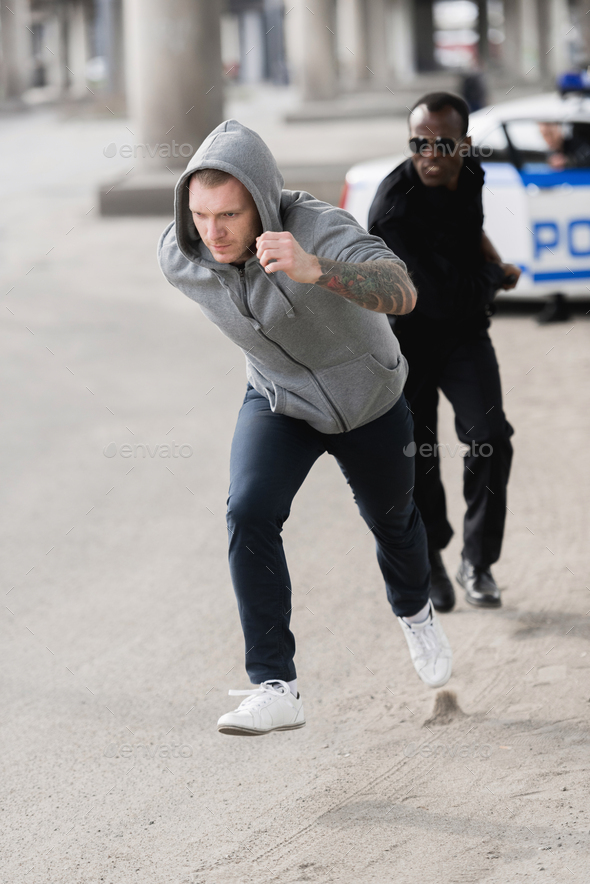 young hooded thief running from african american policeman