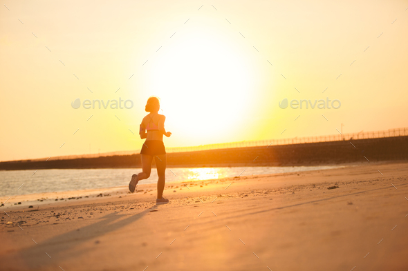 silhouette of female jogger running on beach against sunlight