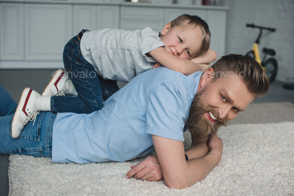 side view of smiling son lying on fathers back at home