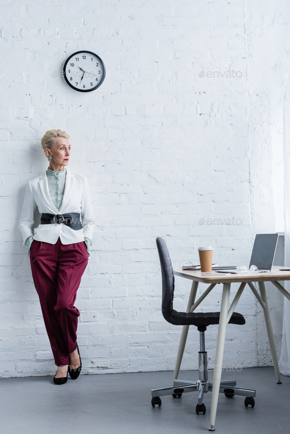 elegant senior businesswoman posing near workplace with laptop and coffee - Stock Photo - Images
