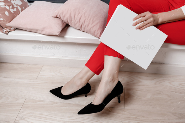 cropped photo of woman hands holding a magazine with mock up. girl in red pants and high heeled