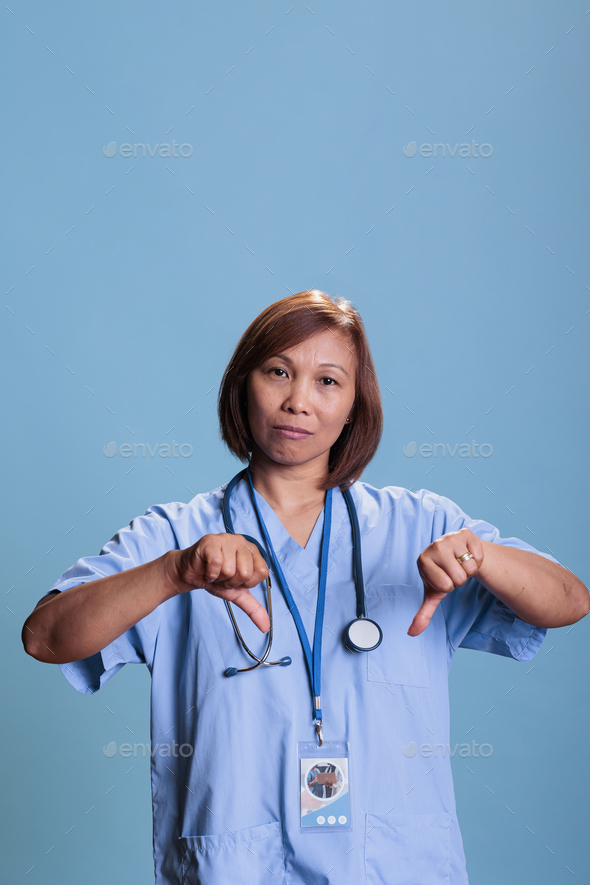 Elderly medical assistant showing thumbs down with a serious look