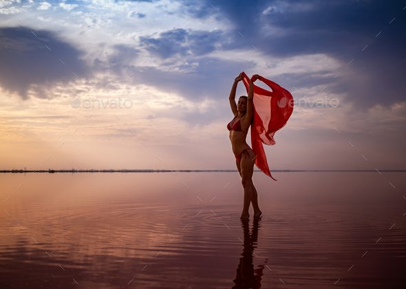 Silhouette of a girl in a red swimsuit on the beach. Red tissue develops in her hands.