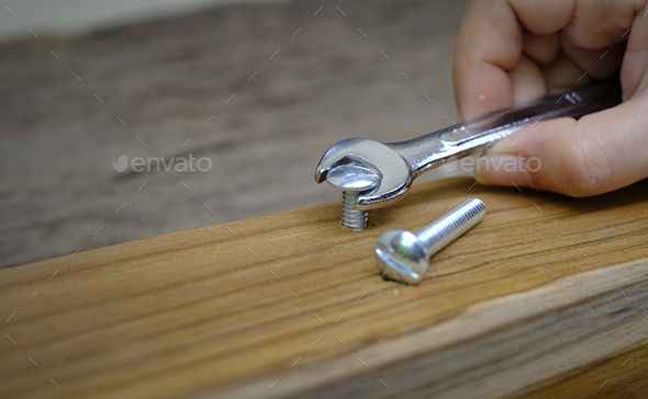 Joiner hand with a wrench screwing nut a furniture screw into a wooden plank