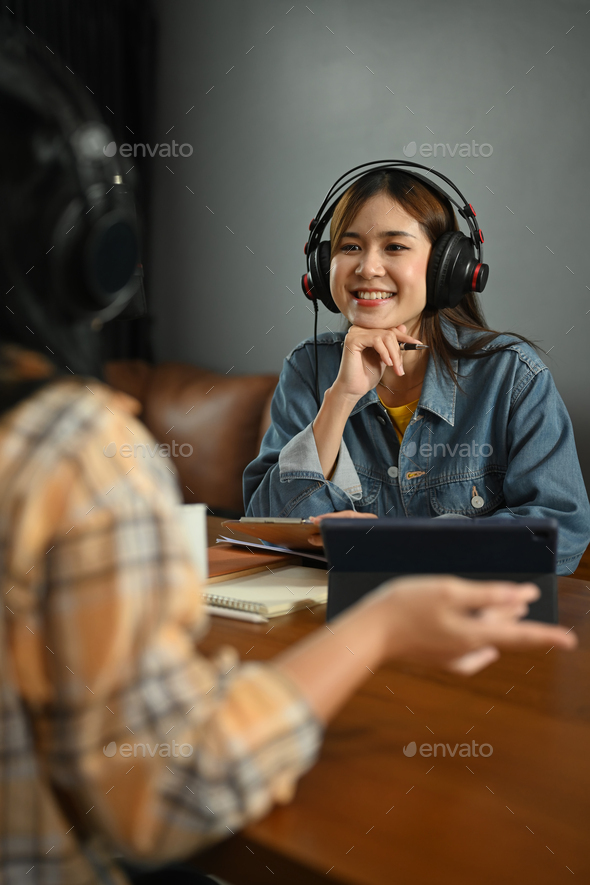 Shot of smiling young female radio host listening to interesting  conversation with guest. Stock Photo by prathanchorruangsak