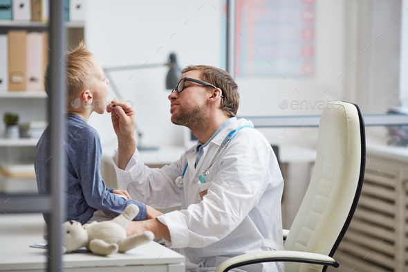 Young pediatrician checking boys throat