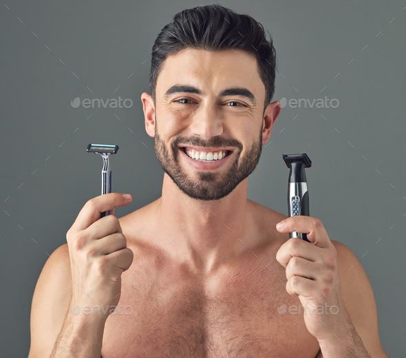 Studio shot of a man holding up a disposable razor and an electric shaver