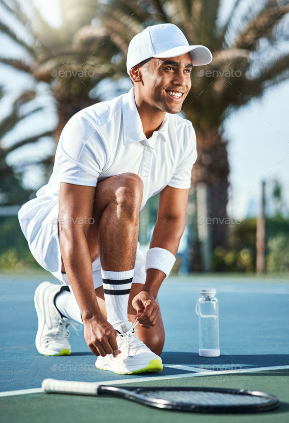 Full length shot of a handsome young man kneeling down to tie his shoelaces before tennis practice