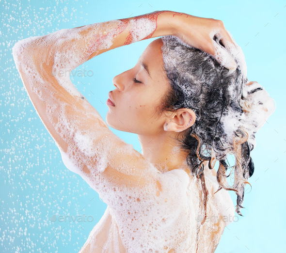 Feeling rejuvenated from head to toes. Shot of a woman washing her hair against a blue background.