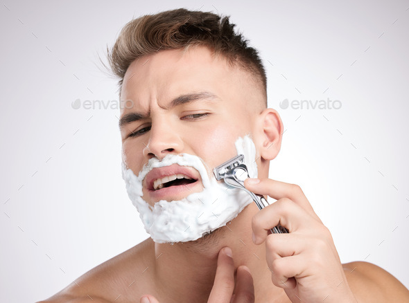 Am I doing it right. Studio shot of a young man shaving his face against a grey background.
